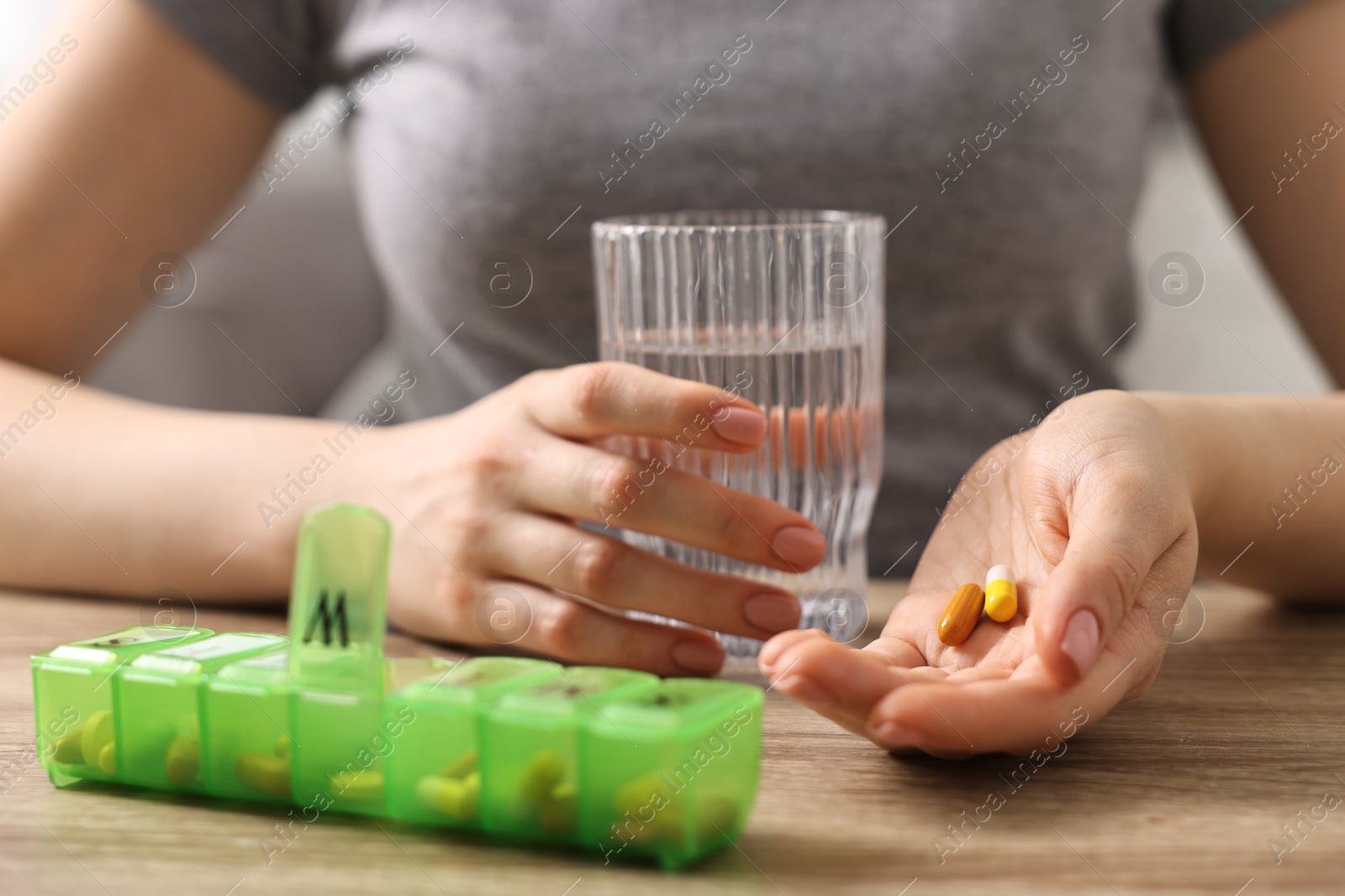 Photo of Woman with pills, organizer and glass of water at wooden table, closeup