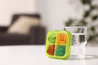 Different pills in organizer and glass of water at white table, closeup. Space for text