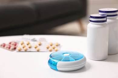 Different pills, organizer and medical jars at white table, selective focus