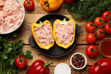 Raw stuffed peppers with ground meat and ingredients on wooden table, flat lay
