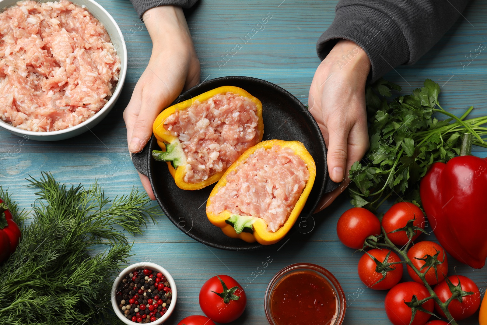 Photo of Woman making stuffed peppers with ground meat at light blue wooden table, top view