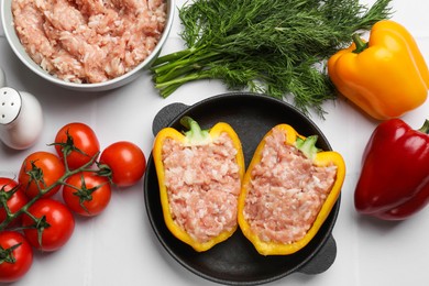 Photo of Raw stuffed peppers with ground meat and ingredients on white tiled table, flat lay