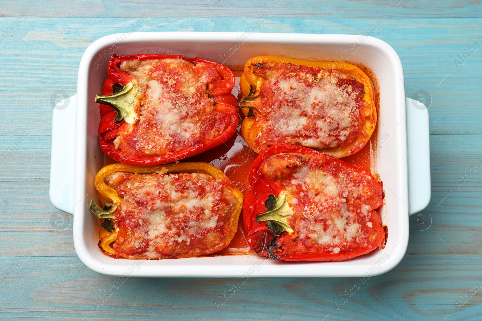 Photo of Tasty stuffed peppers in dish on light blue wooden table, top view