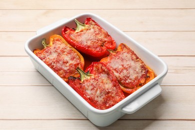 Photo of Tasty stuffed peppers in dish on light wooden table