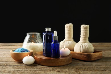 Photo of Spa composition. Cosmetic products, herbal bags, burning candles and sea salt on wooden table against black background