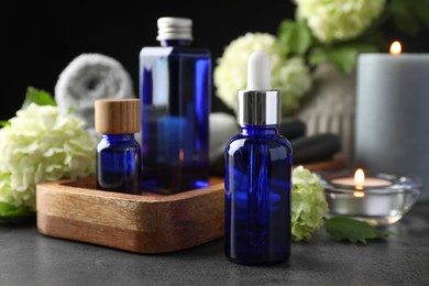 Photo of Spa composition. Cosmetic products, burning candles and hydrangea flowers on gray table, closeup