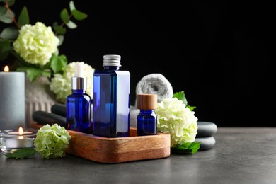 Photo of Spa composition. Cosmetic products, burning candles and hydrangea flowers on gray table against black background, space for text