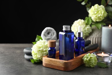 Photo of Spa composition. Cosmetic products, burning candles and hydrangea flowers on gray table against black background, space for text