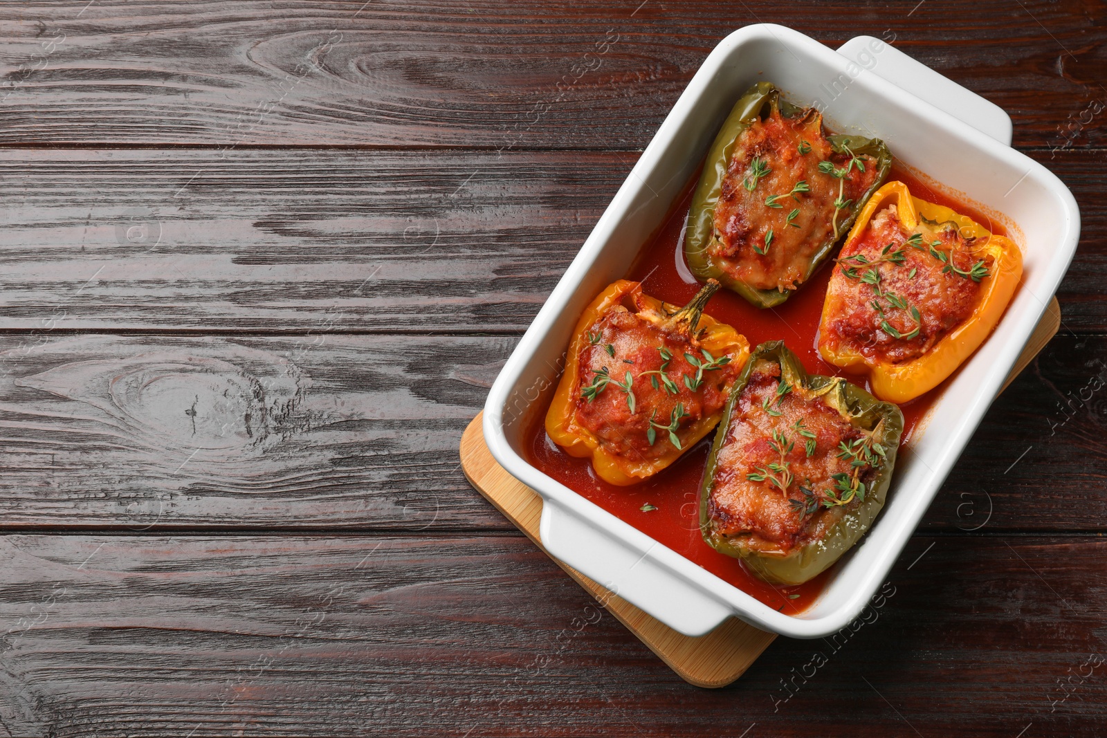 Photo of Tasty stuffed peppers in dish on wooden table, top view. Space for text