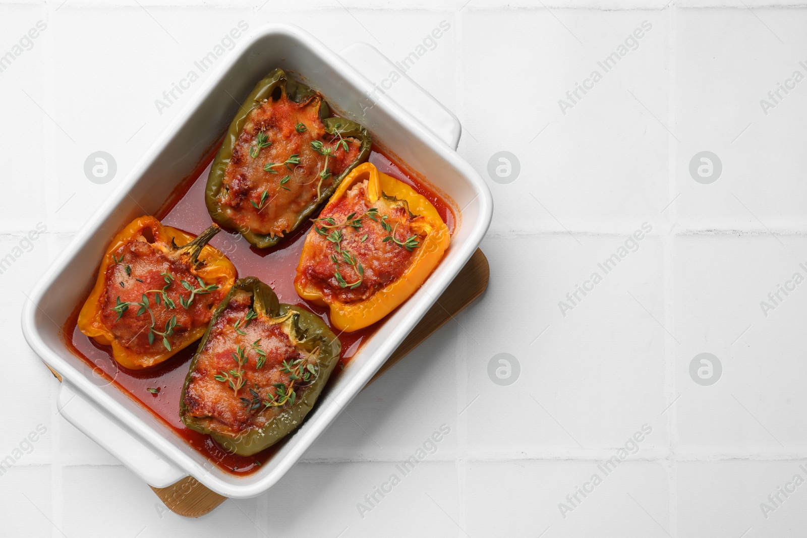 Photo of Tasty stuffed peppers in dish on white tiled table, top view. Space for text