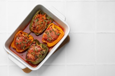 Photo of Tasty stuffed peppers in dish on white tiled table, top view. Space for text