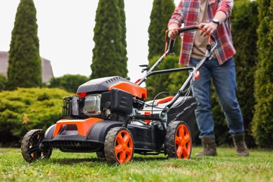 Photo of Man cutting green grass with lawn mower in garden, selective focus