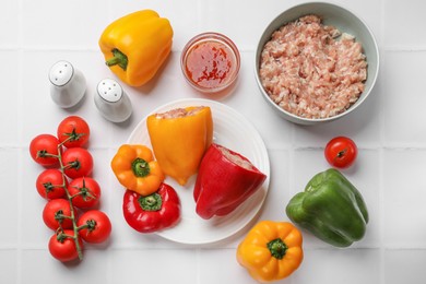 Raw stuffed peppers, ground meat and ingredients on white tiled table, flat lay