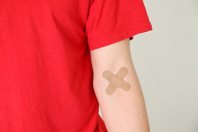 Blood donation. Woman with sticking plaster on her arm against gray background, closeup. Space for text