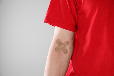Blood donation. Woman with sticking plaster on her arm against gray background, closeup. Space for text