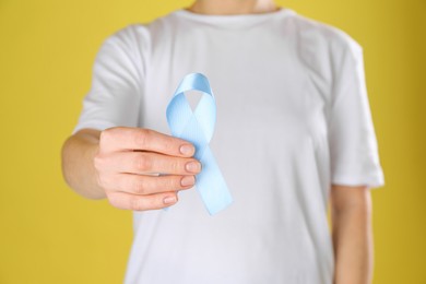 International Psoriasis Day. Woman with light blue ribbon as symbol of support on yellow background, closeup