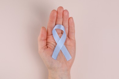 Photo of International Psoriasis Day. Woman with light blue ribbon as symbol of support on beige background, top view