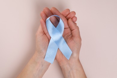 Photo of International Psoriasis Day. Woman with light blue ribbon as symbol of support on beige background, top view
