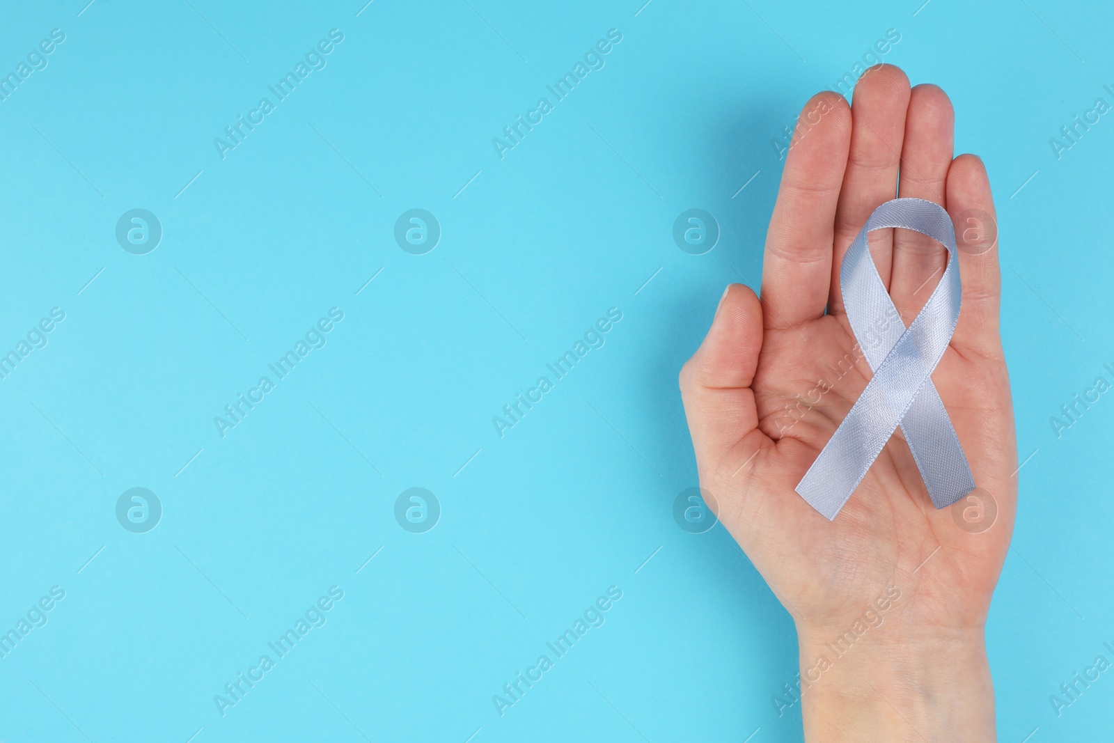 Photo of International Psoriasis Day. Woman with light blue ribbon as symbol of support on light blue background, top view. Space for text