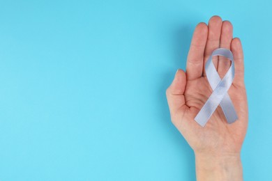 Photo of International Psoriasis Day. Woman with light blue ribbon as symbol of support on light blue background, top view. Space for text