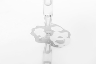 Photo of Glass pipette and transparent liquid on white background, closeup