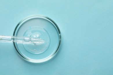 Glass pipette and petri dish with liquid on light blue background, top view