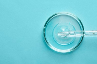 Photo of Glass pipette and petri dish with liquid on light blue background, top view. Space for text