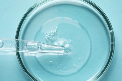 Glass pipette and petri dish with liquid on light blue background, top view