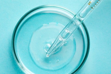 Photo of Glass pipette and petri dish with liquid on light blue background, top view