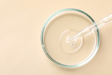 Glass pipette and petri dish with liquid on beige background, top view. Space for text