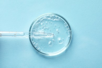 Glass pipette and petri dish with liquid on light blue background, top view