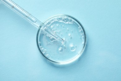 Glass pipette and petri dish with liquid on light blue background, top view