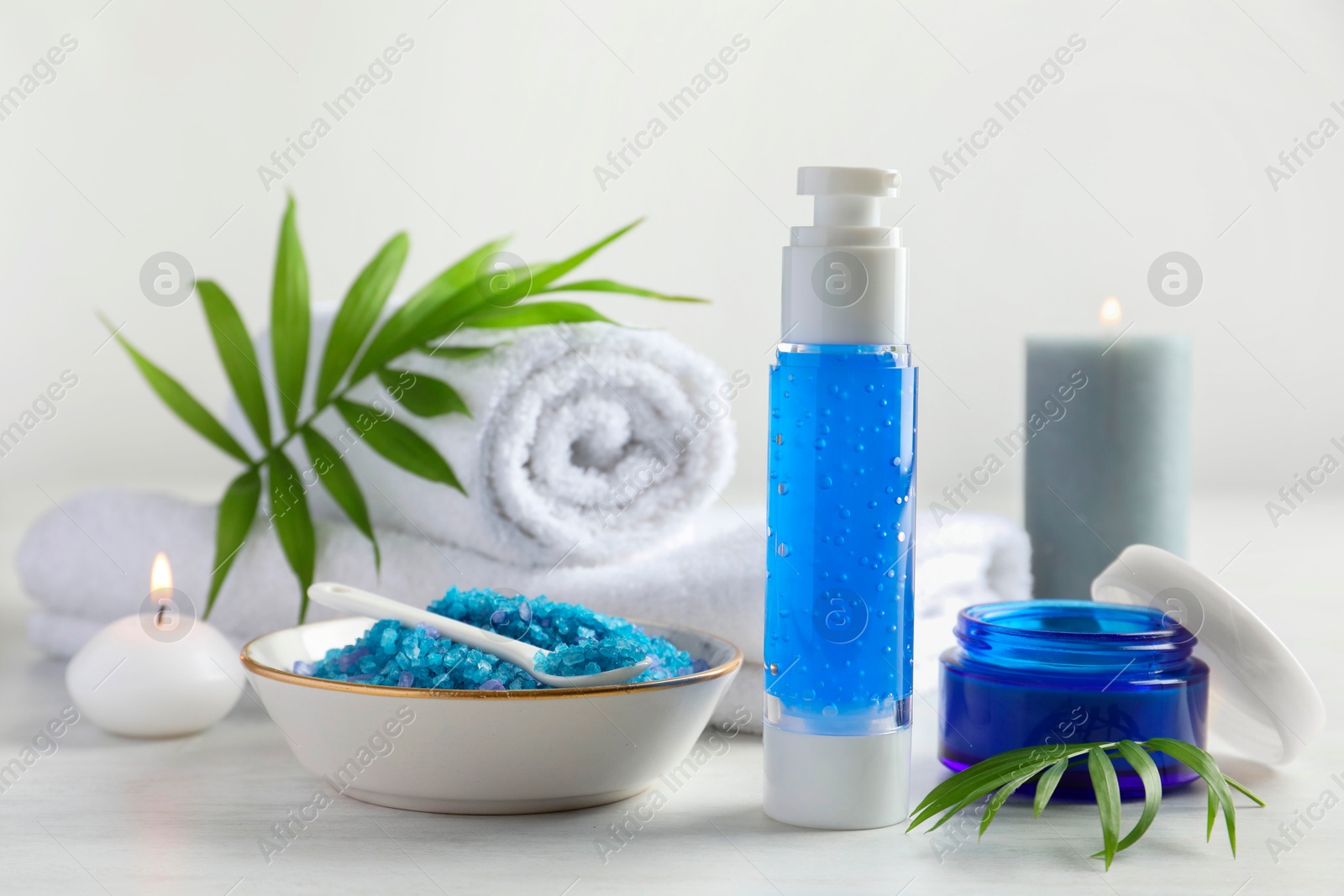 Photo of Spa composition. Cosmetic products, sea salt, towels and burning candles on light table