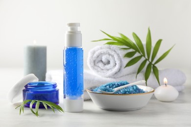 Photo of Spa composition. Cosmetic products, sea salt, towels and burning candles on light table