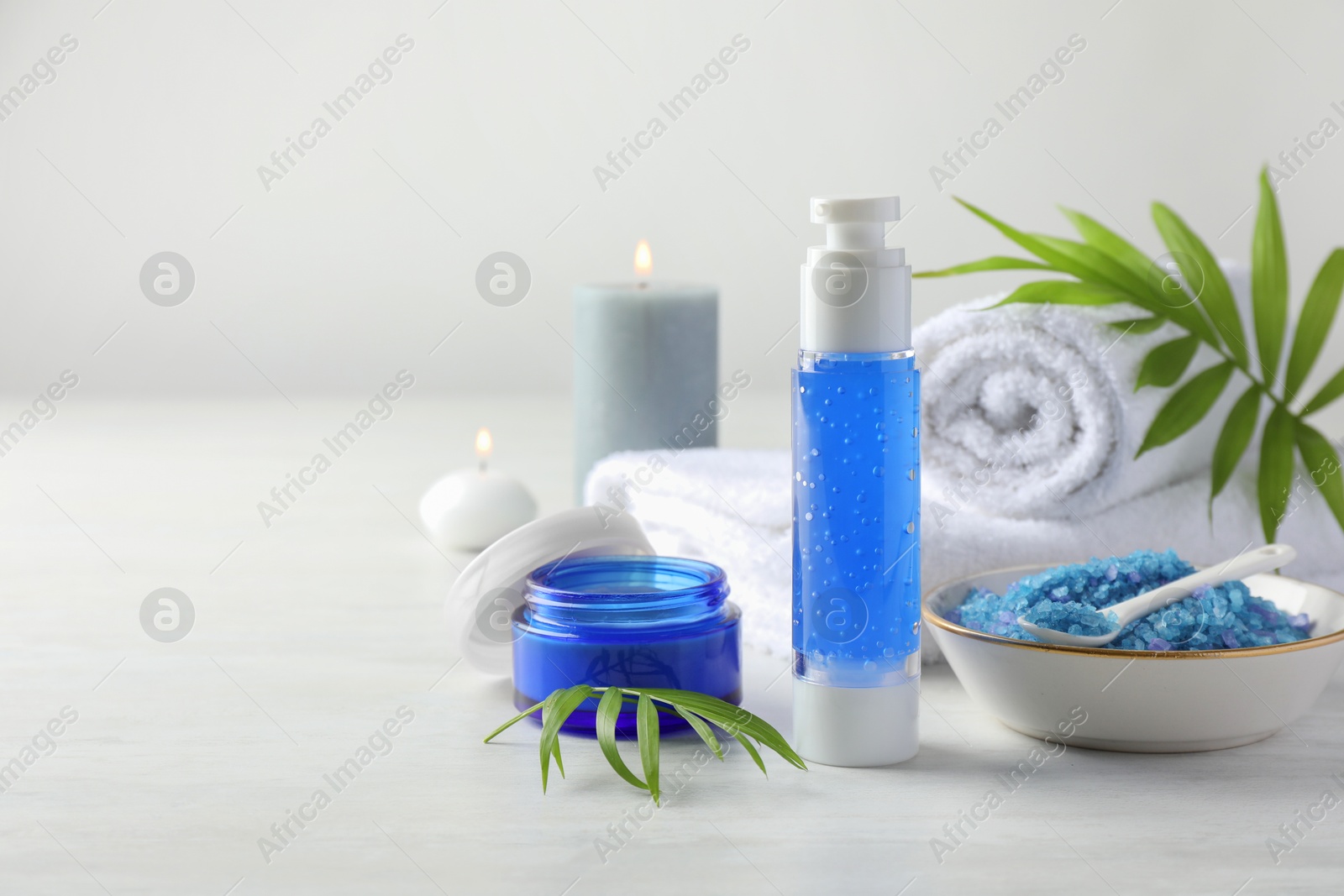 Photo of Spa composition. Cosmetic products, sea salt, towels and burning candles on light table, space for text