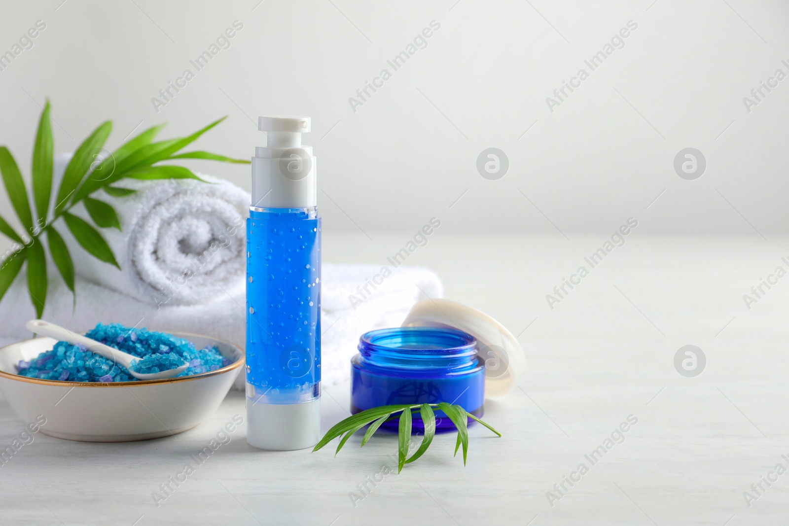 Photo of Spa composition. Cosmetic products, sea salt and towels on light table, space for text