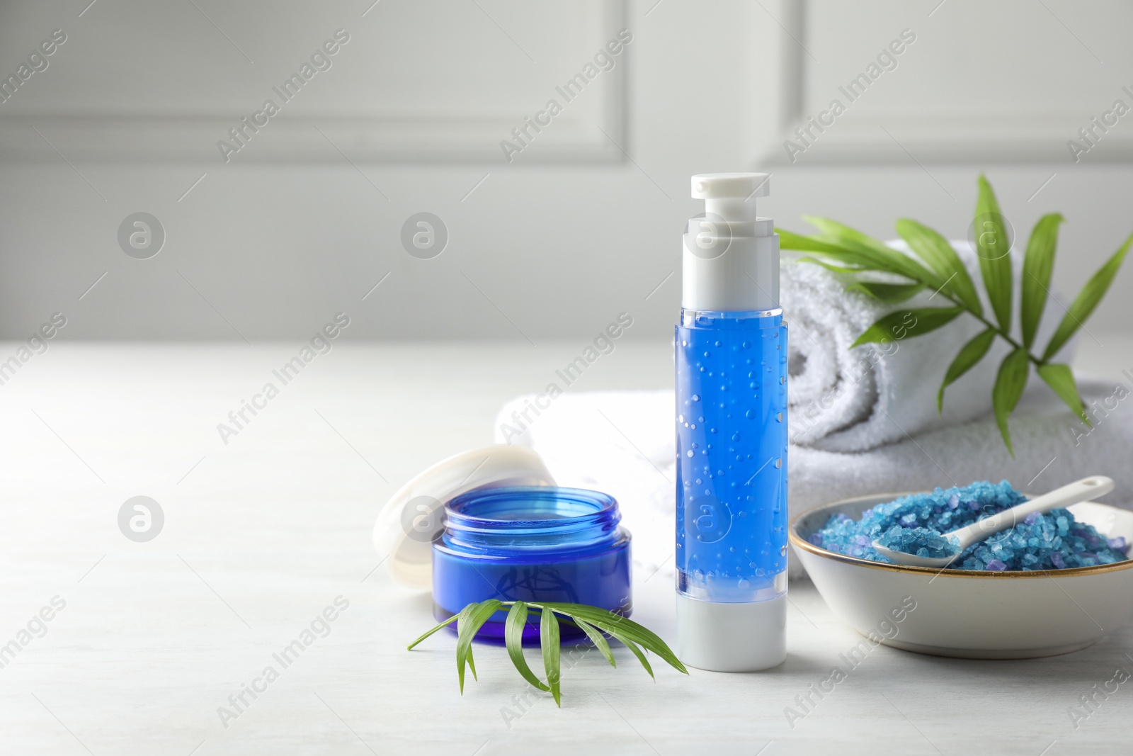 Photo of Spa composition. Cosmetic products, sea salt and towels on light table, space for text