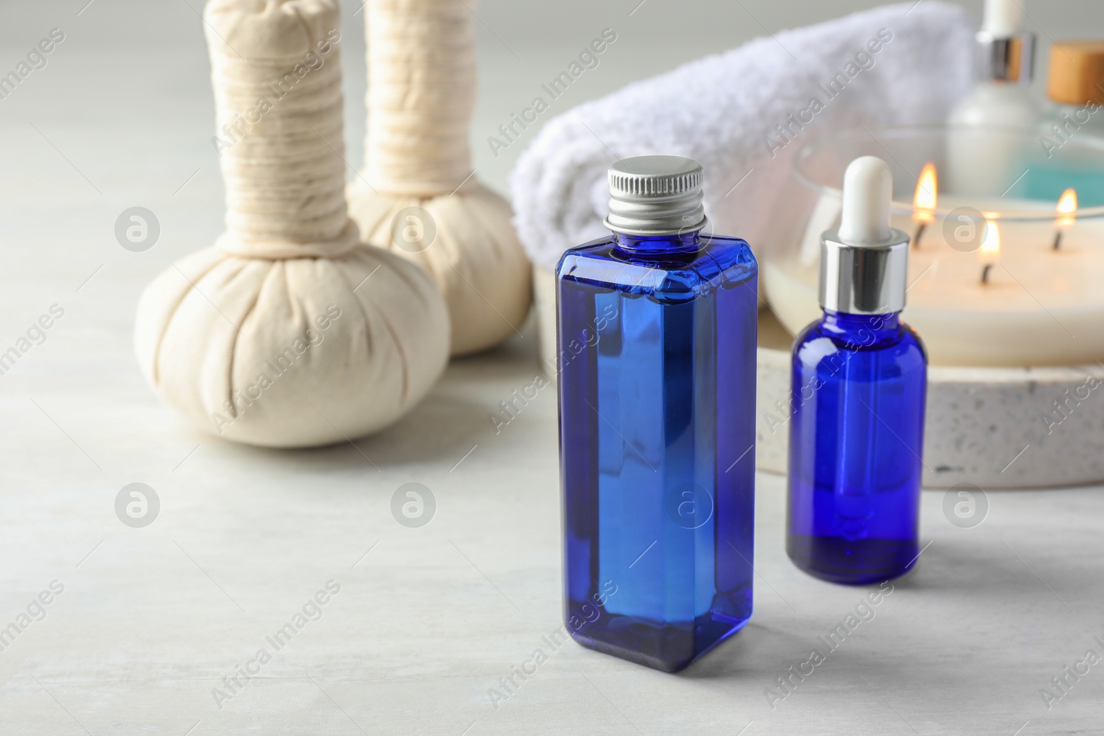 Photo of Spa composition. Bottles of cosmetic products, herbal bags, towel and burning candle on wooden table