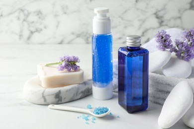 Photo of Spa composition. Bottles of cosmetic products, sea salt, stones, soap and flowers on white marble table