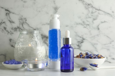 Spa composition. Bottles of cosmetic products, dry flowers and burning candles on white marble table