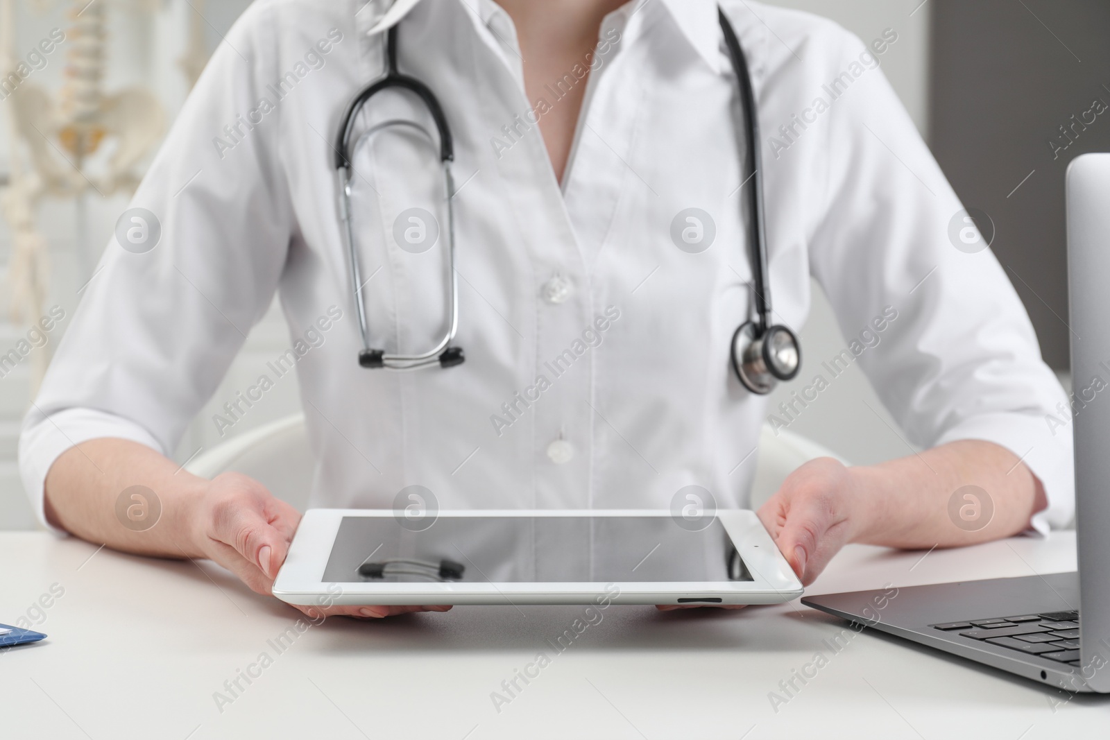Photo of Doctor with tablet at white table in clinic, closeup