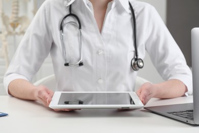 Doctor with tablet at white table in clinic, closeup
