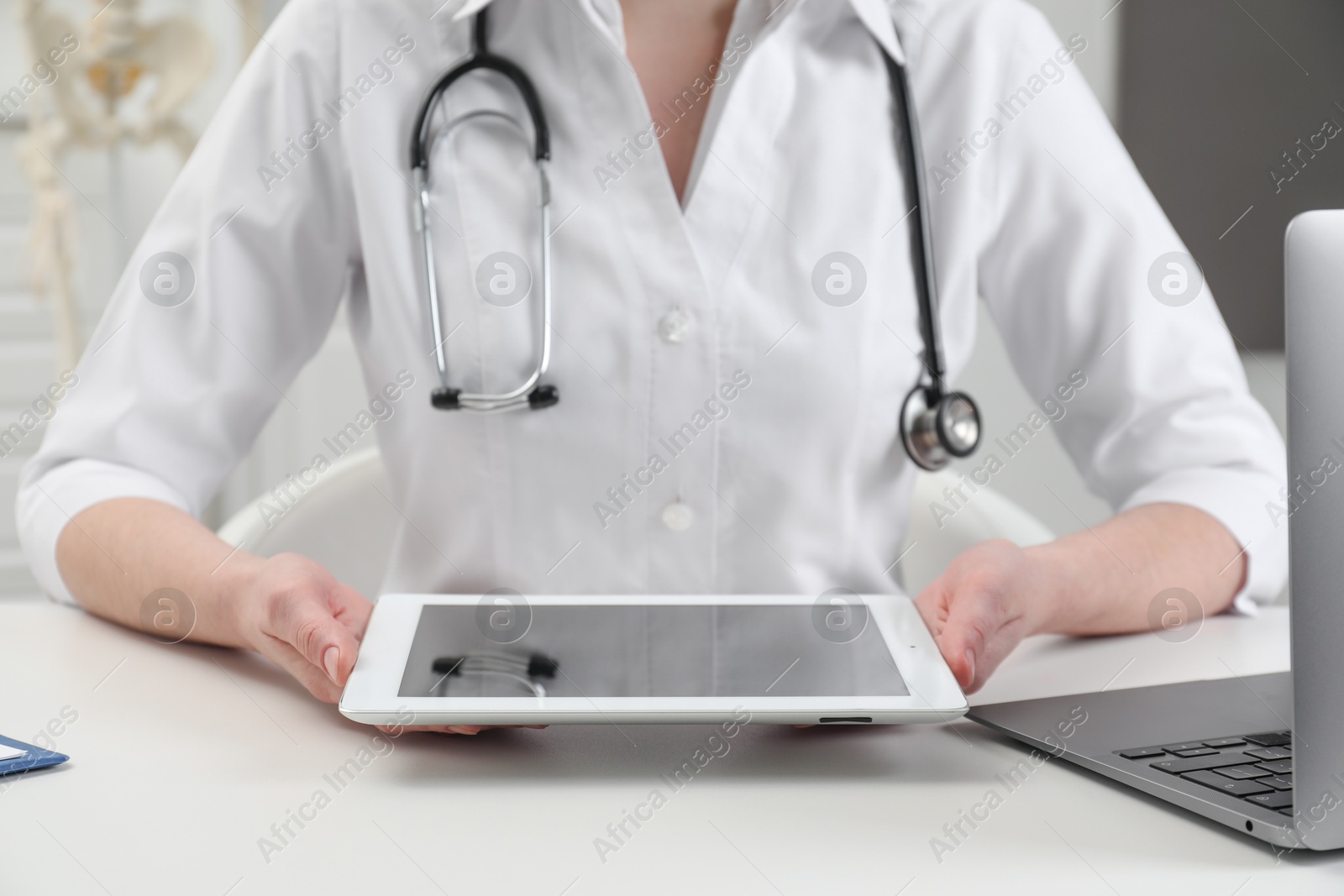 Photo of Doctor with tablet at white table in clinic, closeup