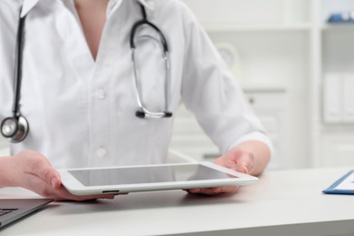 Photo of Doctor with tablet at white table in clinic, closeup