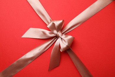 Photo of Beige satin ribbon with bow on red background, closeup