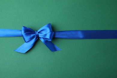 Blue satin ribbon with bow on green background, top view