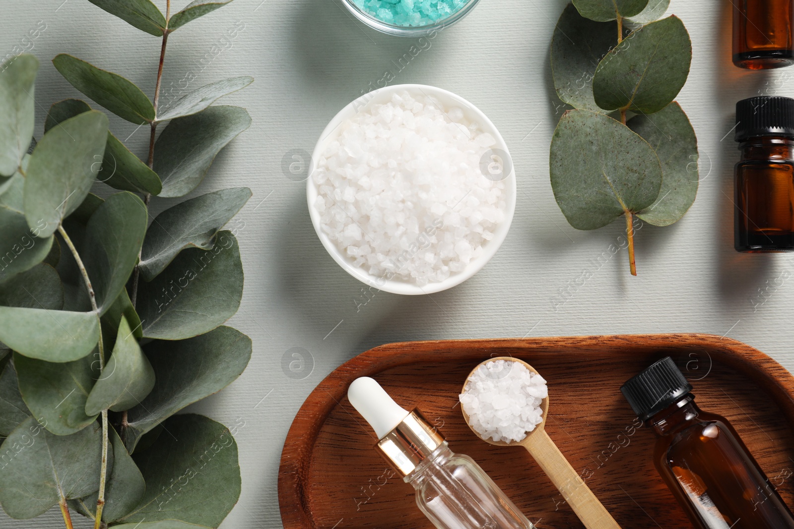 Photo of Aromatherapy products. Bottles of essential oil, sea salt and eucalyptus branches on grey background, flat lay