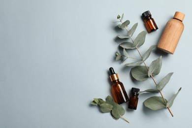 Photo of Aromatherapy. Bottles of essential oil and eucalyptus leaves on light grey background, flat lay. Space for text