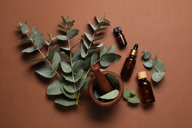 Aromatherapy. Bottles of essential oil, mortar and eucalyptus branches on brown background, flat lay