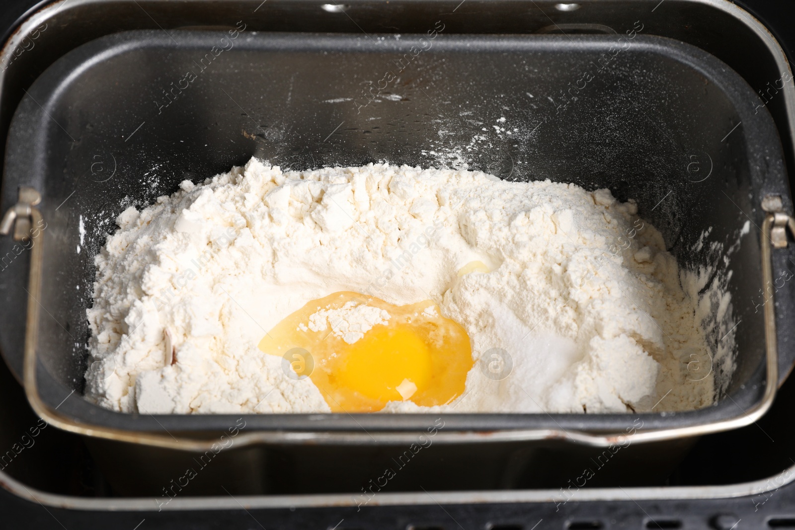 Photo of Making dough. Flour and egg in breadmaker pan, closeup